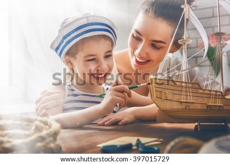 Mother and her child girl making model ship. Dreams of sea, adventures and travel.