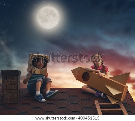Children on the background of moon sky. Child boy in an astronaut costume and child girl with toy rocket standing on the roof of the house and looking at the sky and dreaming of becoming a spacemen.