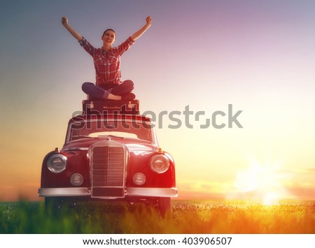 Toward adventure! Girl relaxing and enjoying road trip. Beautiful young woman sitting on roof of vintage car.