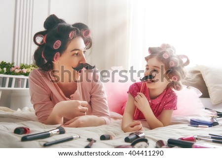 Funny family! Mother and her child daughter girl with a paper accessories. Mother and daughter preparing for a party and having fun. Beautiful young woman and funny girl with a paper mustache on stick