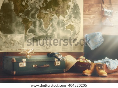 travel preparation. suitcase, clothing and accessories in vintage style on the background of wooden wall and maps of the world.
