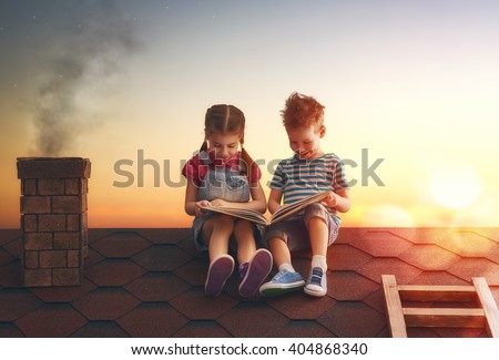 Children reading a book sitting on the roof of the house. Boy and girl reading by the light of sunset.