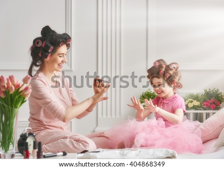 Happy loving family. Mother and daughter are doing hair, manicures and having fun. Mother and daughter sitting on the bed in the bedroom.