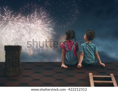 Two cute children sit on the roof and look at the fireworks.