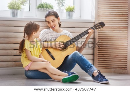Happy family. Mother and daughter playing guitar together. Adult woman playing guitar for child girl.