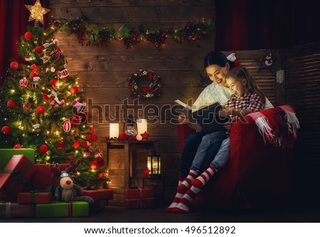 Merry Christmas! Pretty young mother reading a book to her daughter near Christmas tree.