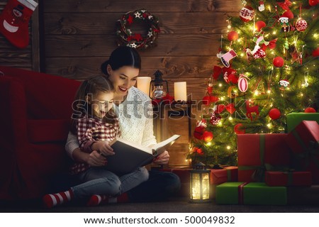 Merry Christmas! Pretty young mother reading a book to her daughter near Christmas tree.
