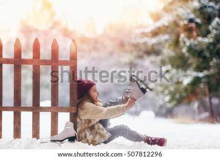 Happy child playing on a winter walk in nature. Cute little kid girl is going skate outdoors.