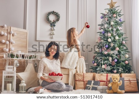 Merry Christmas and Happy Holidays!  Mom and daughter decorate the Christmas tree in room. Loving family indoors.