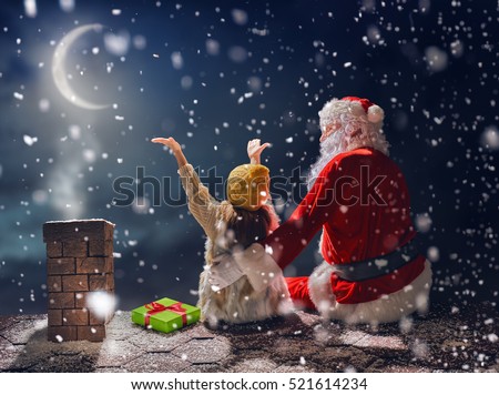 Merry Christmas and happy holidays! Cute little child girl and Santa Claus sitting on the roof and looking at snowfall. Christmas legend concept.