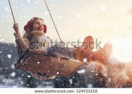 Happy child girl on swing in sunset winter. Little kid playing on a winter walk in nature.