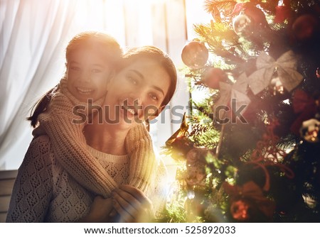 Merry Christmas and Happy Holidays! Mom and daughter decorate the Christmas tree indoors. The morning before Xmas. Portrait loving family close up.