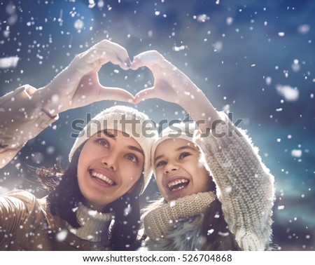 Happy loving family! Mother and child girl having fun, playing and laughing on snowy winter walk in nature. Frost winter season. Mom and kid making hand heart in evening.