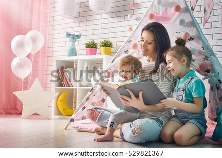 Happy loving family. Pretty young mother reading a book to her daughters indoors. Funny mom and lovely child having fun in children room.