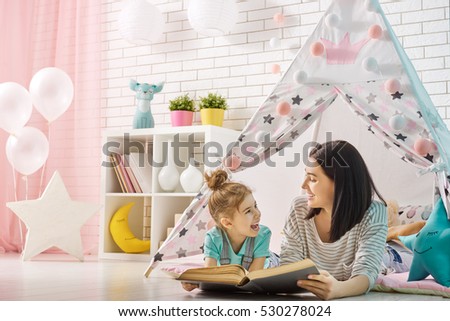 Happy loving family. Pretty young mother reading a book to her daughter indoors. Funny mom and lovely child having fun in children room.