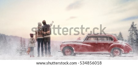 Toward adventure! Happy family relaxing and enjoying road trip. Mom, dad, child and vintage car on snowy winter nature background. Christmas holidays time.