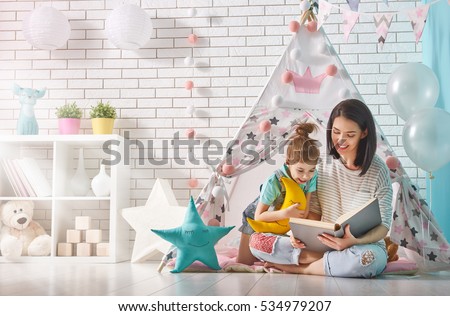 Happy loving family. Pretty young mother reading a book to her daughter indoors. Funny mom and lovely child having fun in children room.
