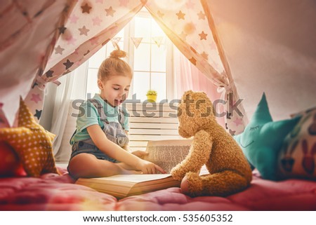 Cute little child girl is reading a book. Happy girl play at home. Funny lovely child having fun in children room.