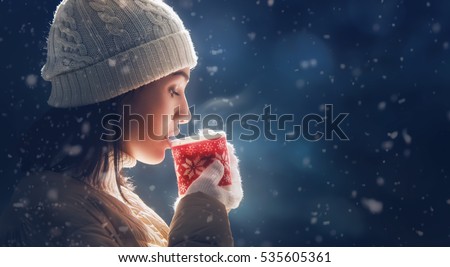 Happy young woman with a cup of hot tea on snowy winter walk in nature. Concept of frost winter season.