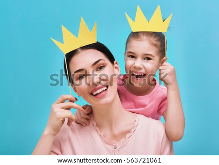 Funny family on a background of bright blue wall. Mother and her daughter girl with a paper accessories. Mom and child are holding crown on stick.