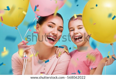 Funny family on a background of bright blue wall. Mother and her daughter girl are having fun with balloons and confetti. Yellow, pink and turquoise colors.
