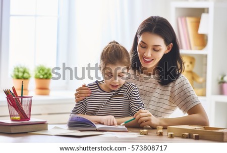 Pretty young mother and her cute daughter are reading a book. Learning to read at home.