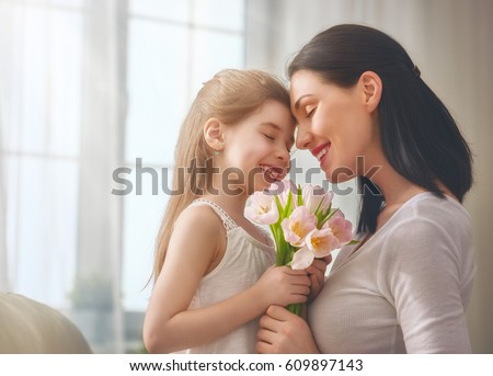 Happy mother\'s day! Child daughter congratulates mom and gives her flowers tulips. Mum and girl smiling and hugging. Family holiday and togetherness.