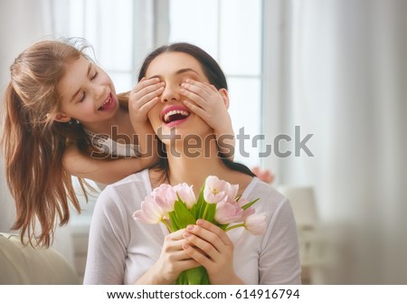 Happy mother\'s day! Child daughter congratulates mom and gives her flowers tulips. Mum and girl smiling and hugging. Family holiday and togetherness.