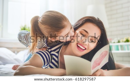 Happy mother\'s day! Child daughter congratulates mom and gives her postcard. Mum and girl smiling and hugging. Family holiday and togetherness.