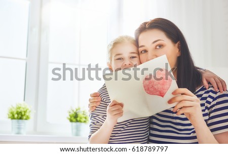 Happy mother\'s day! Child daughter congratulates mom and gives her postcard. Mum and girl smiling and hugging. Family holiday and togetherness.