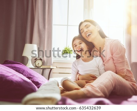 A nice girl and her mother enjoy sunny morning. Good time at home. Child wakes up from sleep. Family playing on the bed in the bedroom.