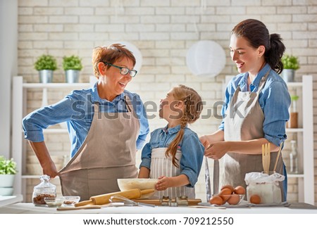 Happy loving family are preparing bakery together. Granny, mom and child daughter girl are cooking cookies and having fun in the kitchen. Homemade food and little helper.