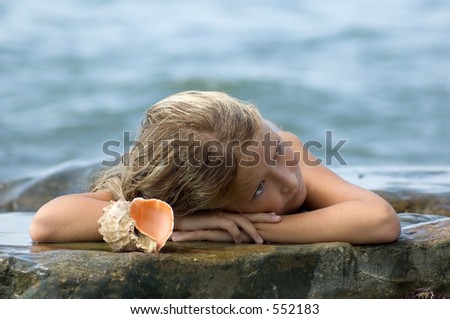 Dreaming little girl like a mermaid laying on the rock with seashell