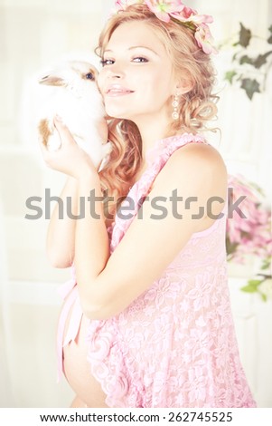 Portrait of young beautiful blond pregnant woman wearing in pink with white rabbit and pink flowers on her head. with long curly hair.