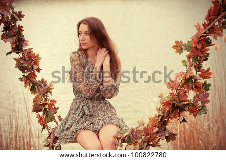 Autumn mood. Beautiful woman sitting on the swing decorated with garland of autumn leaves