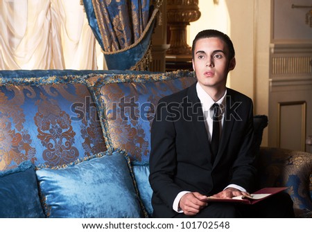Young brunet man in blue royal interior, sitting on the sofa.