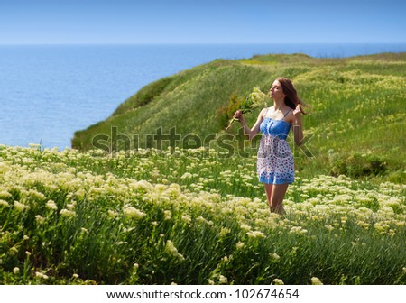 Smiling pretty woman walking among the blooming flowers. Green hills  and the sea. Woman smelling the flowers.