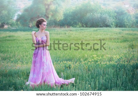 Romantic portrait of young woman in airy pink dress on a countryside background