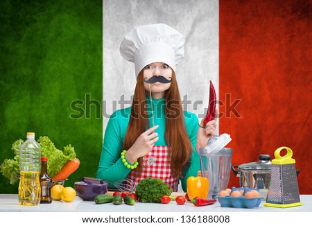 Humorous portrait of a woman in chef\'s hat with paper mustache  holding the paprika in the kitchen with the italian flag on the background. Italian cuisine.