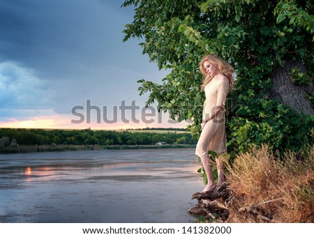 Portrait of a beautiful sad woman on the riverside at sunset