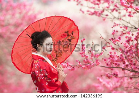 Asian style portrait of a woman with red umbrella, flowering tree branches background