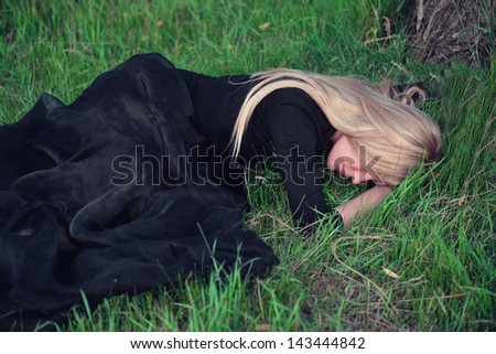 Sad blond woman in black dress lying on the grass