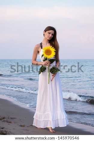 Woman in white dress with sunflower in her hands posing for photo at the beach