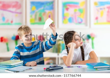 Smiling boy with a paper plane and bored girl sitting by the table