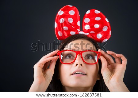 Surprised girl with a big hair bow and glasses looking up. Close-up portrait, black background