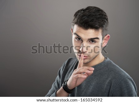 Studio Portrait Of A Young Man Making A Silence Gesture, Gray Background