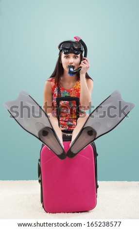 Funny portrait of a girl going on a vacation with her travel luggage and snorkeling equipment, on blue background