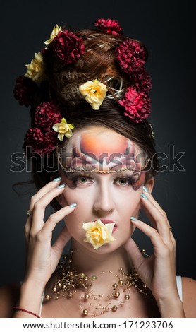 Portrait of a woman in art make-up and hair style with flower in her mouth, dark background