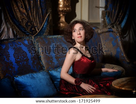 Portrait of a woman in red cocktail dress sitting on blue sofa in luxury interior