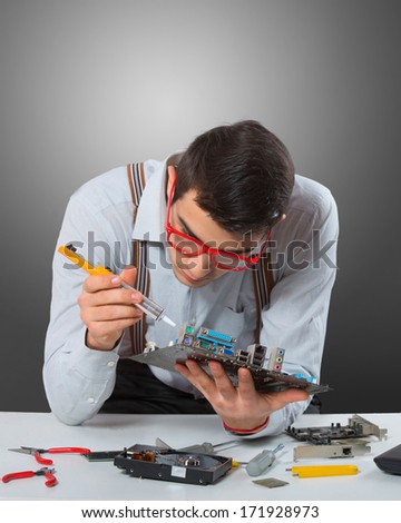 Man in red-framed glasses fixing a computer mother board, gray background